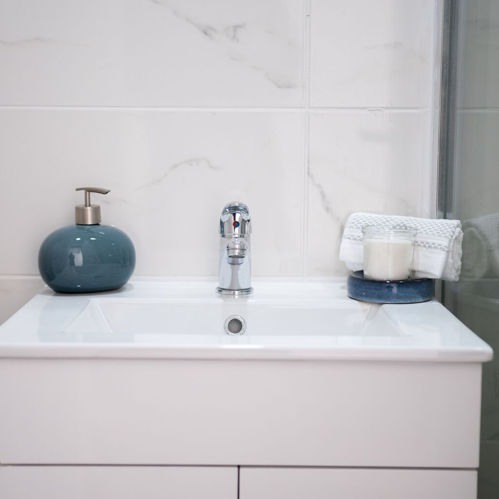 White bathroom cabinet with a tiled background and silver taps.