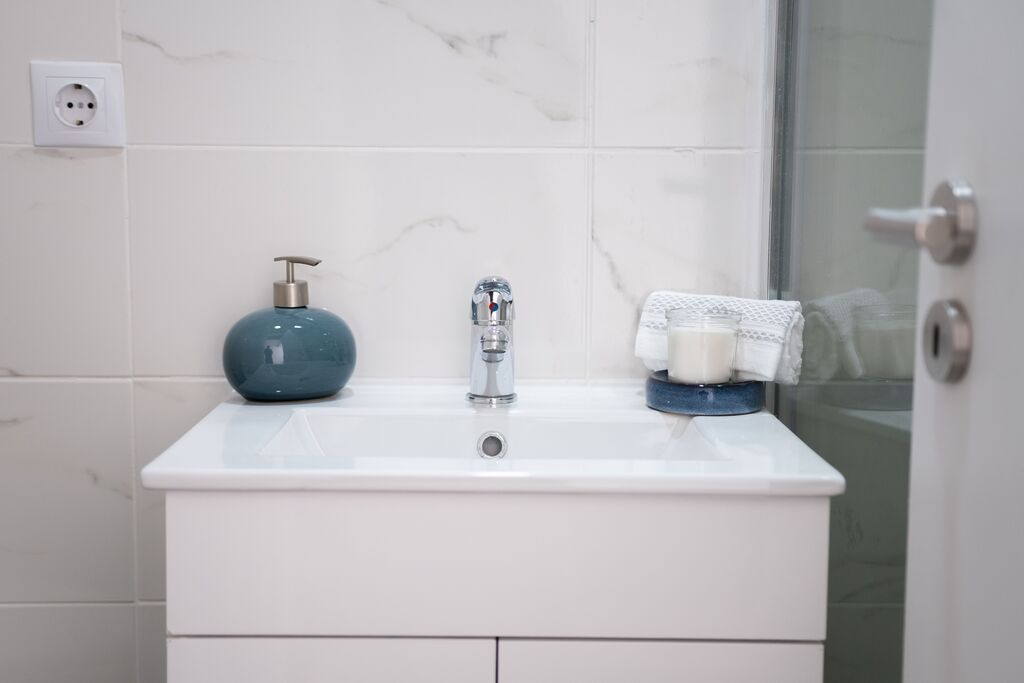 White bathroom cabinet with a tiled background and silver taps.